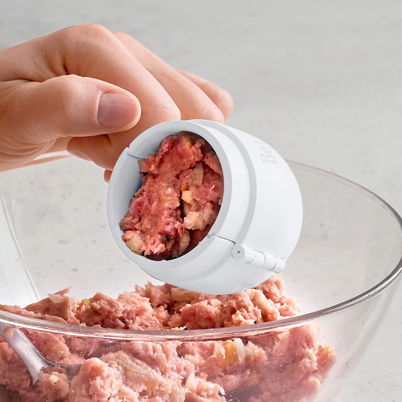 Fleischbällchen-Former mit Fleisch in einer Schüssel, Nahaufnahme, Hand hält Werkzeug