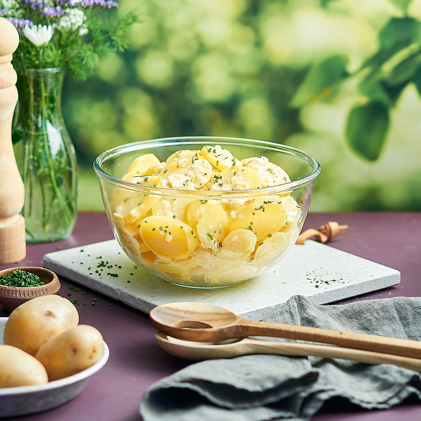 Kartoffelsalat in Glasschüssel mit Kräutern und Zutaten auf Tisch