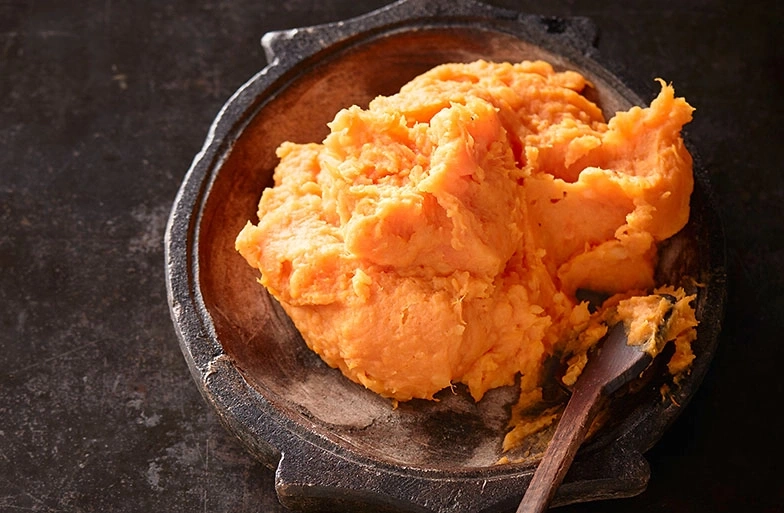 Nahaufnahme von Süßkartoffelpüree in einer Schüssel mit einem Löffel.