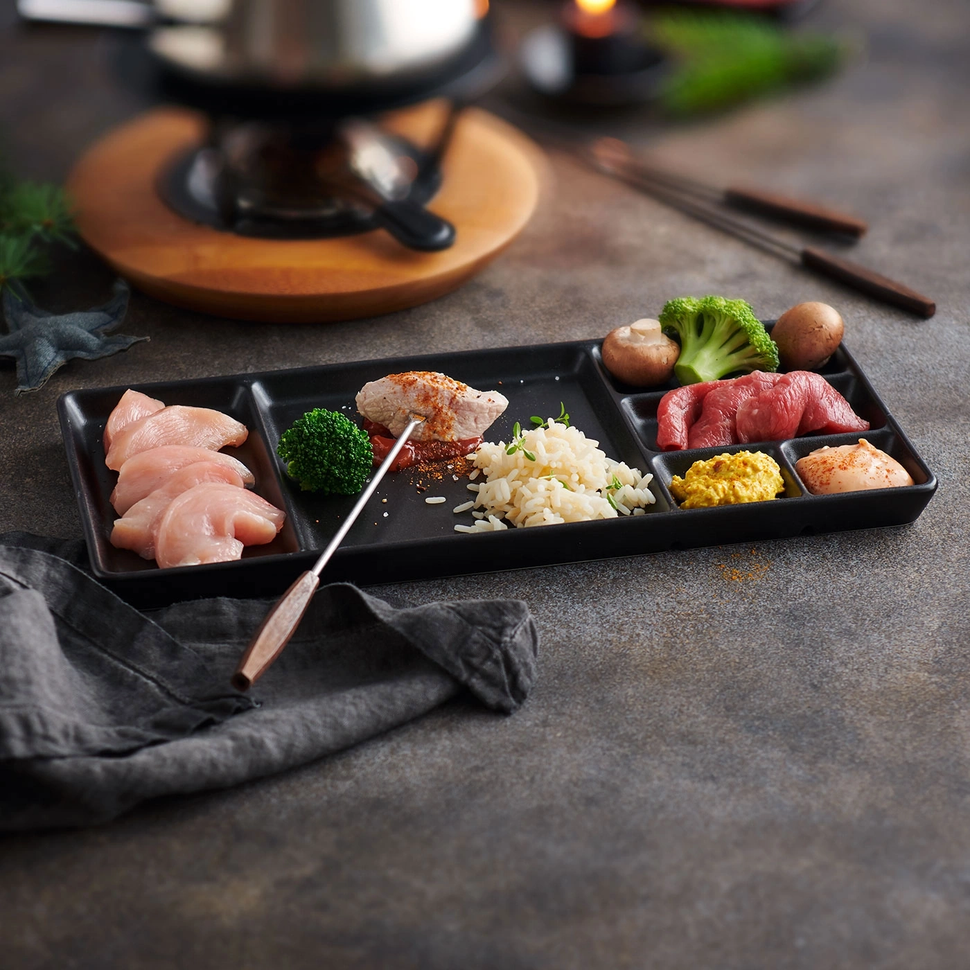 Ingrédients de fondue sur plateau: viandes, légumes, riz et sauces.