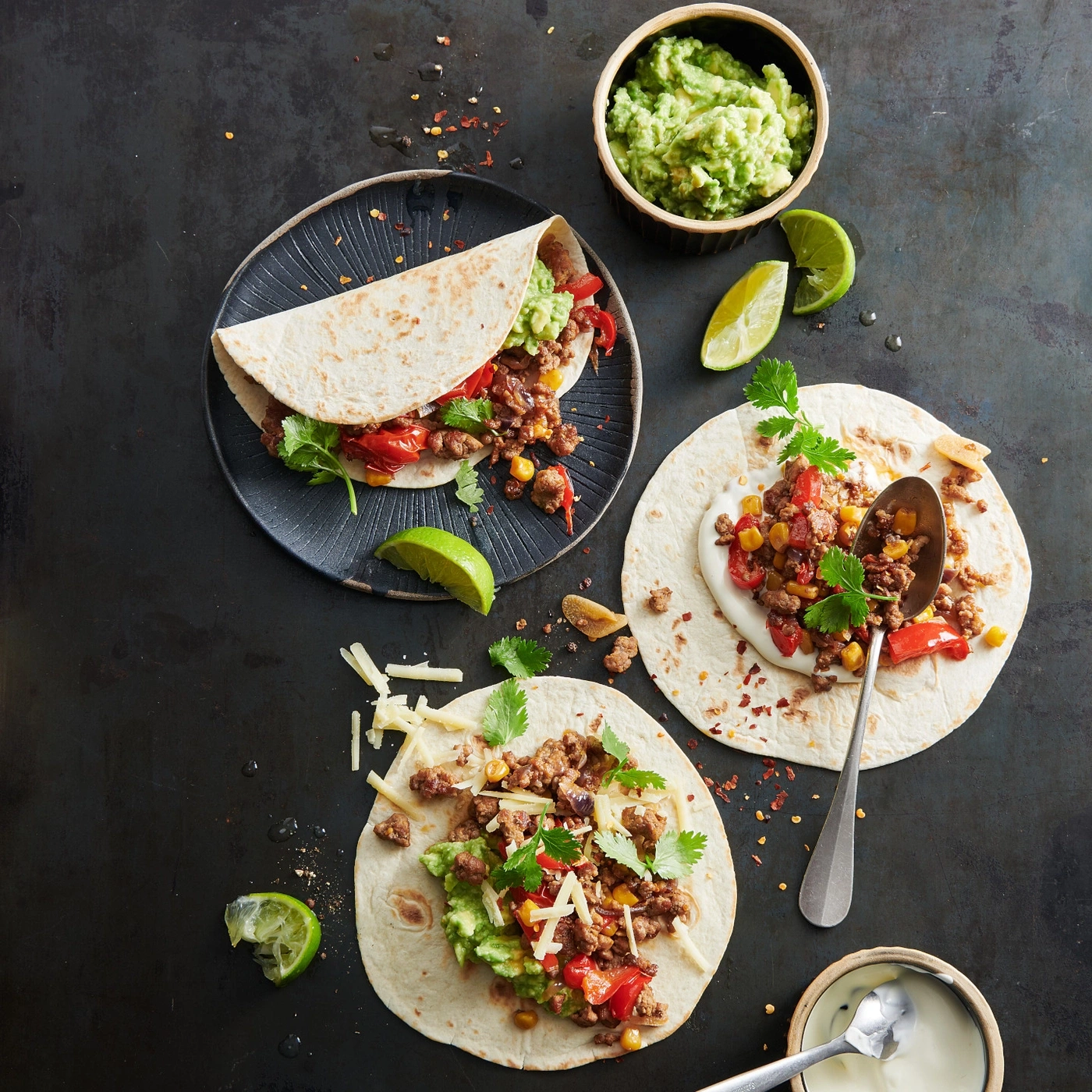 Tacos mit Fleisch, Guacamole, Limetten und Käse auf dunklem Hintergrund