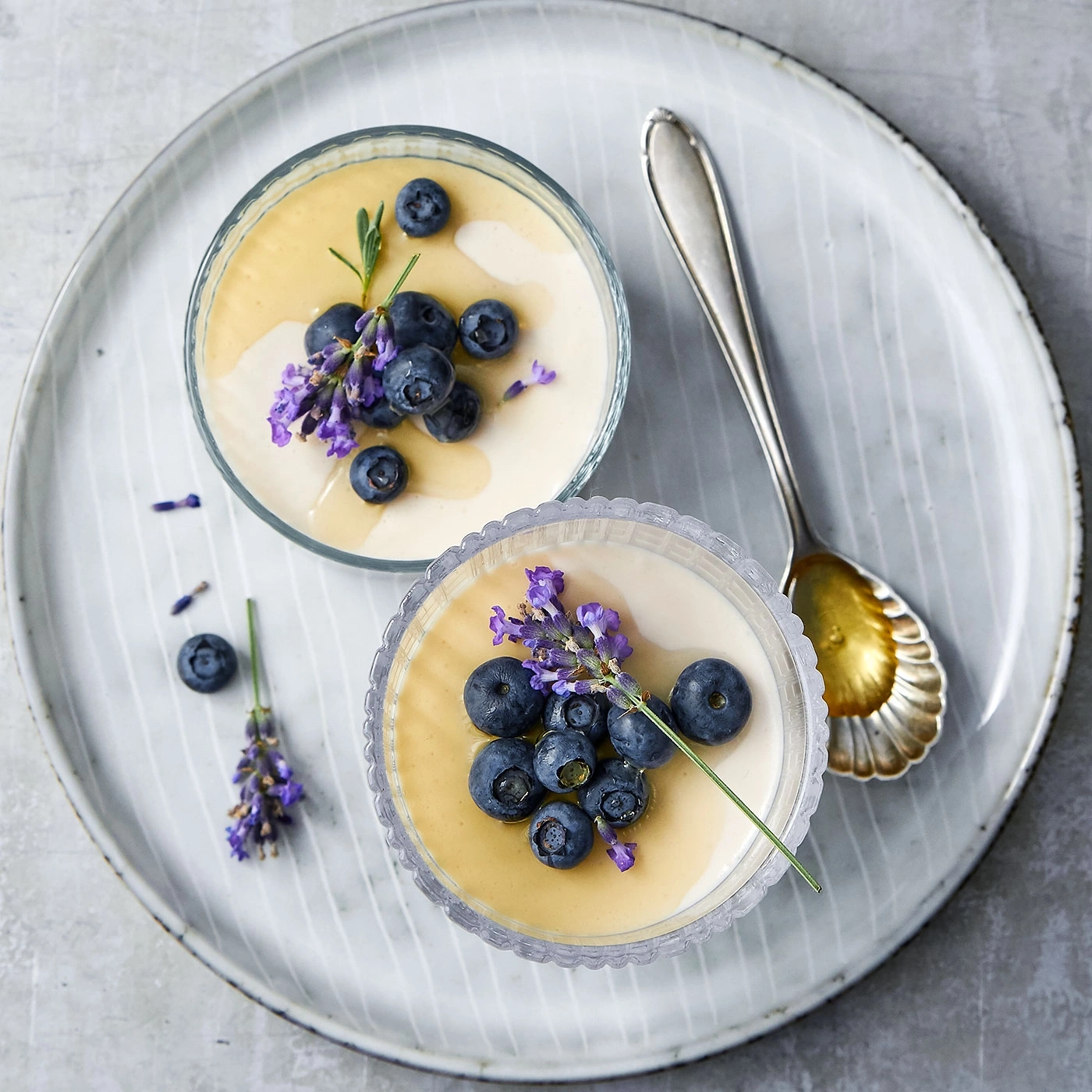 Zwei Desserts mit Blaubeeren und Lavendel auf einem Teller mit Löffel.