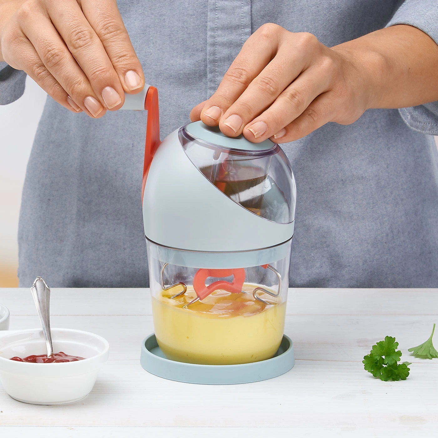 Une personne utilise un mélangeur manuel pour mélanger un liquide jaune, avec du ketchup.