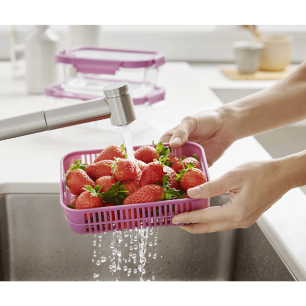 Des fraises sont lavées dans une passoire rose sous l'eau courante.