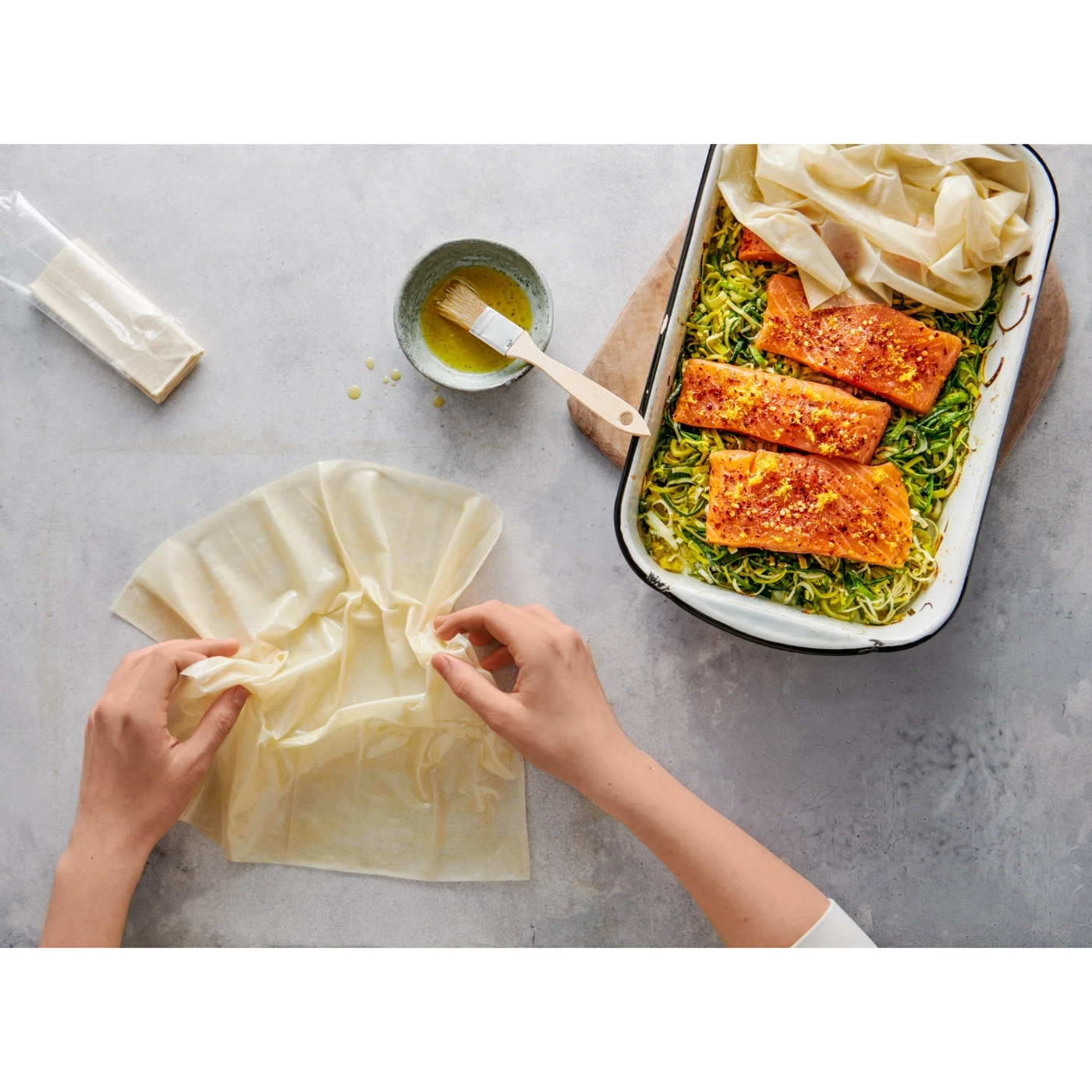 Person bereitet Essen zu, Lachs in Auflaufform, Filoteig, Öl, Pinsel