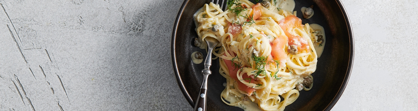 Pasta mit Lachs, Kapern und Dill in einer dunklen Schüssel auf grauem Hintergrund