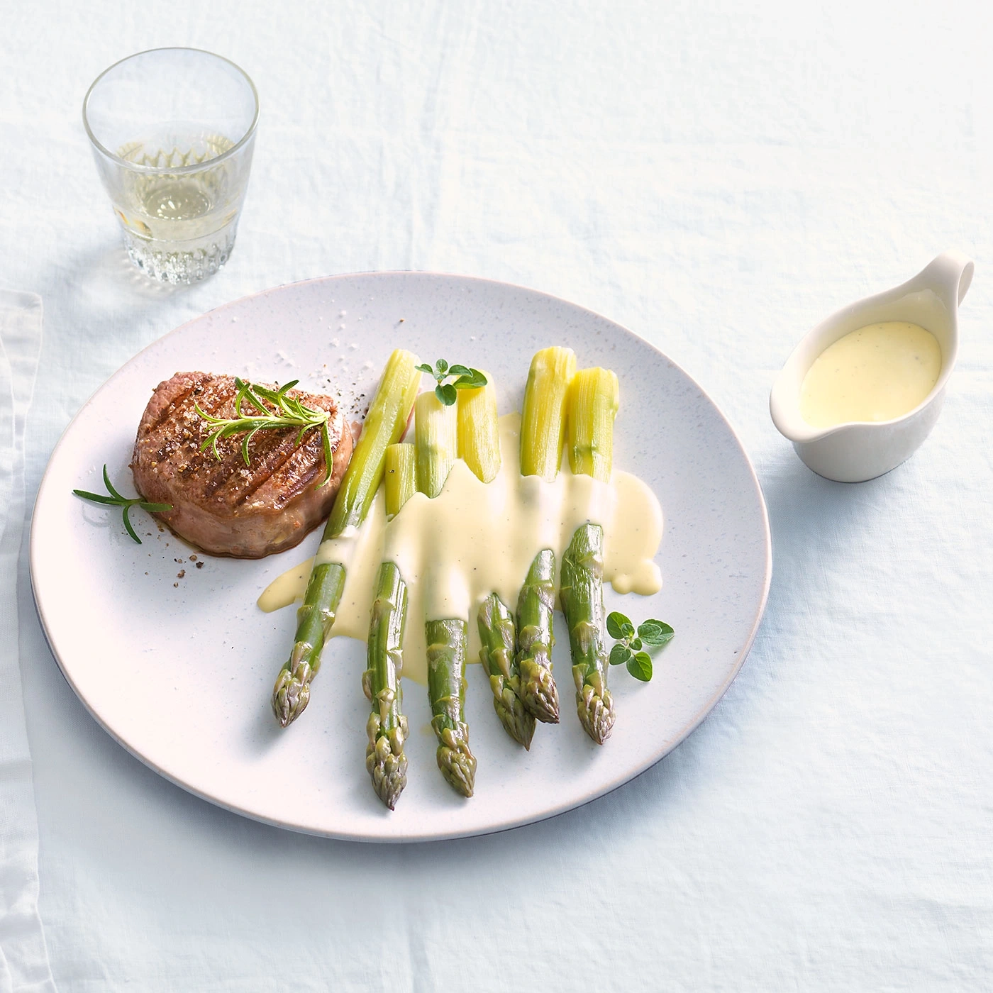 Steak, asperges et sauce sur une assiette, verre de vin.