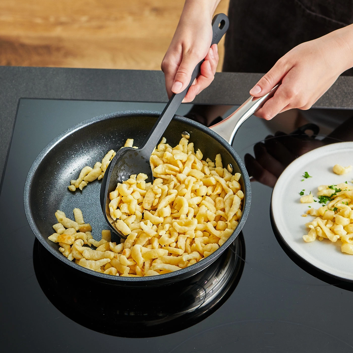 Person kocht Spätzle in einer Pfanne und serviert sie auf einem Teller.