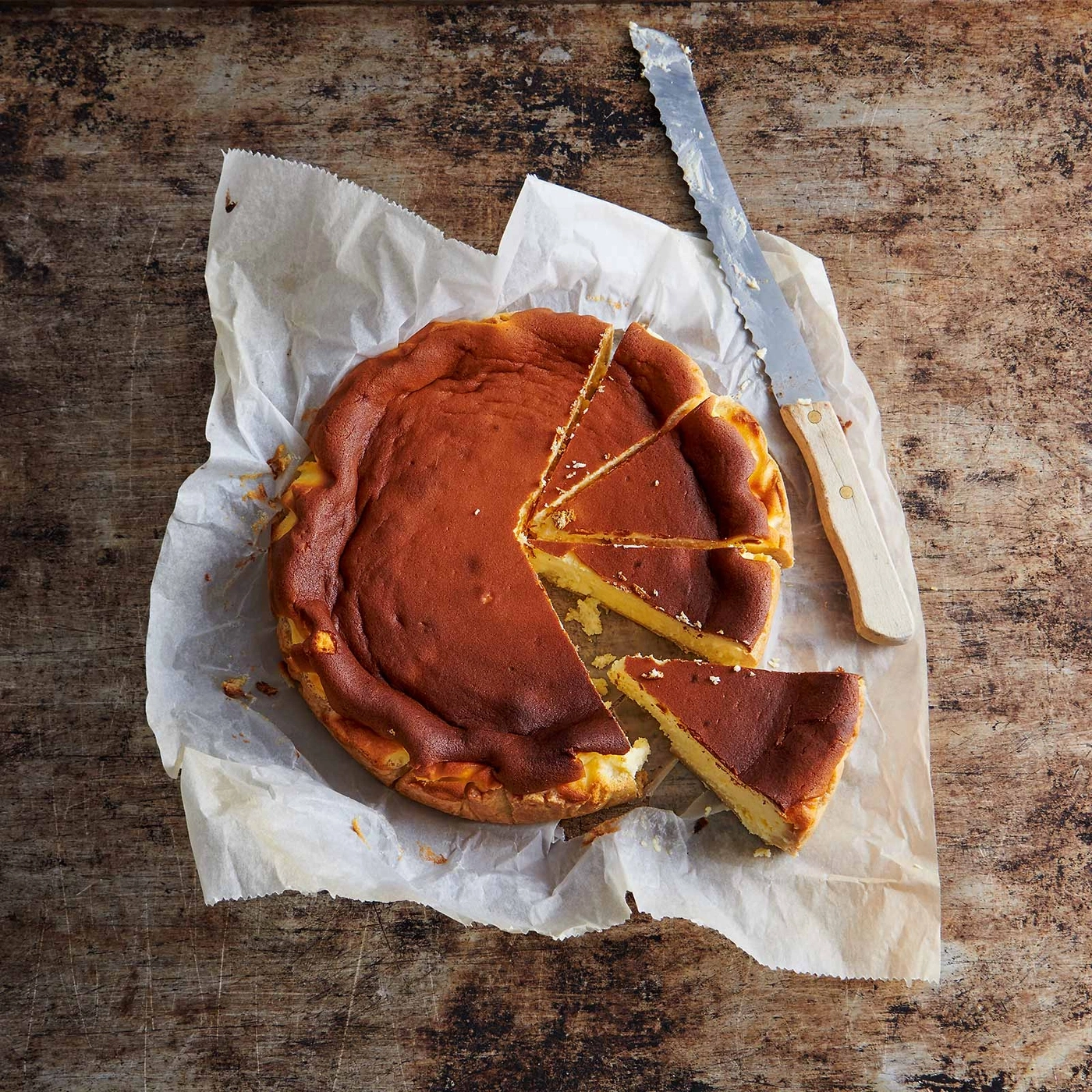 Käsekuchen auf Papier mit Messer auf Holzuntergrund, angeschnitten
