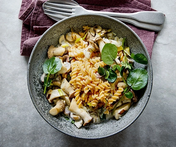 Pasta-Gericht mit Pilzen und Kräutern in einer Schüssel auf einem Tisch