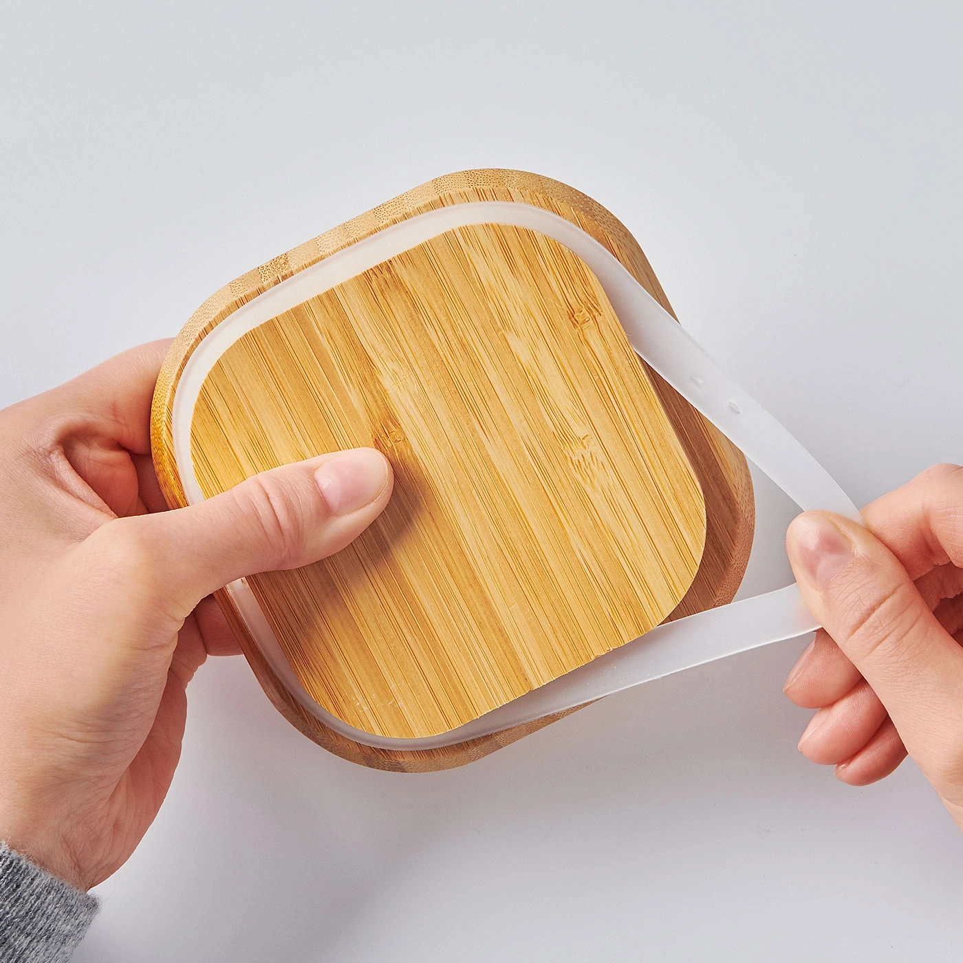Personne ouvrant une boîte à lunch en bambou avec une bande de silicone blanche.