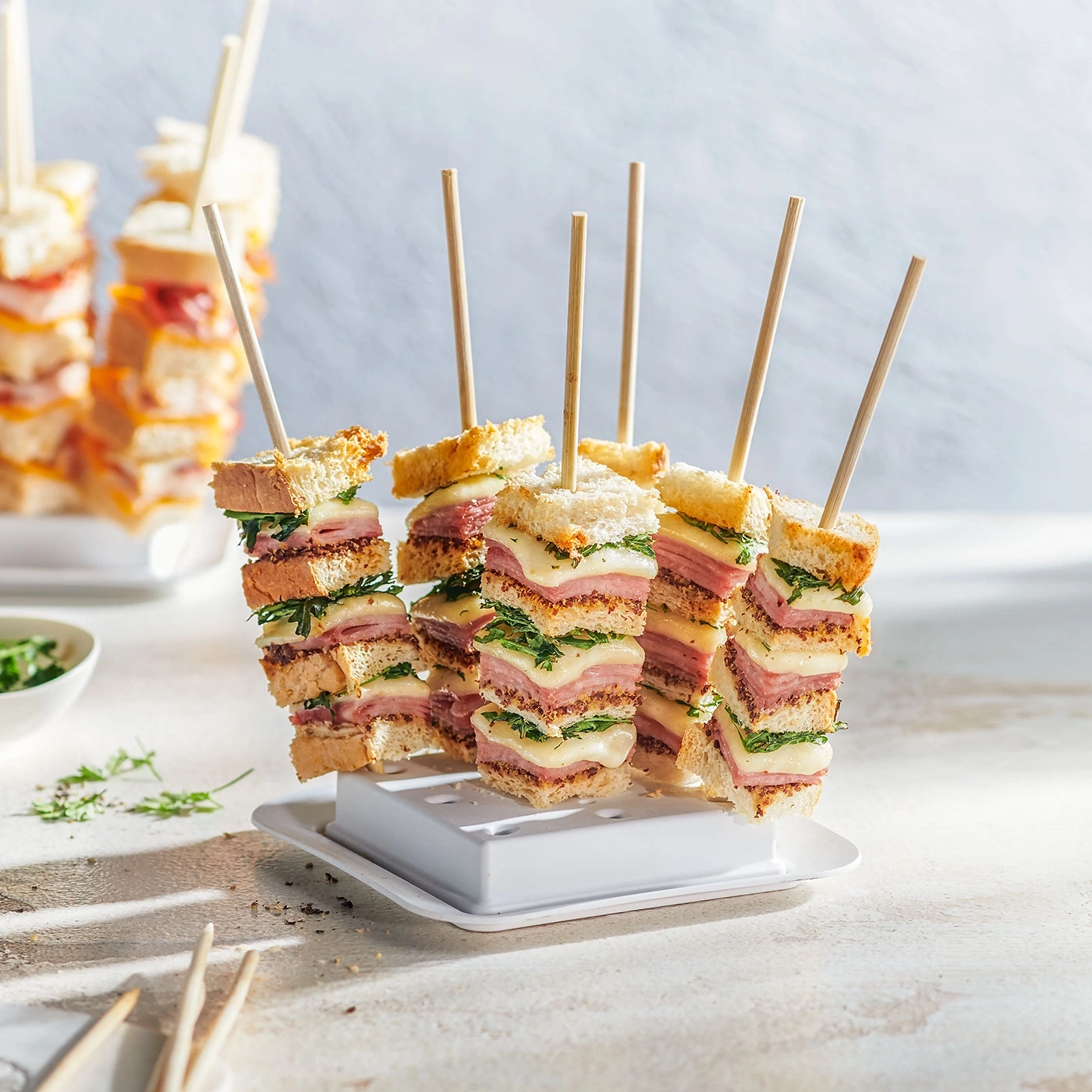 Kleine Sandwich-Spieße mit Käse, Schinken und Brot, auf einem weißen Teller.