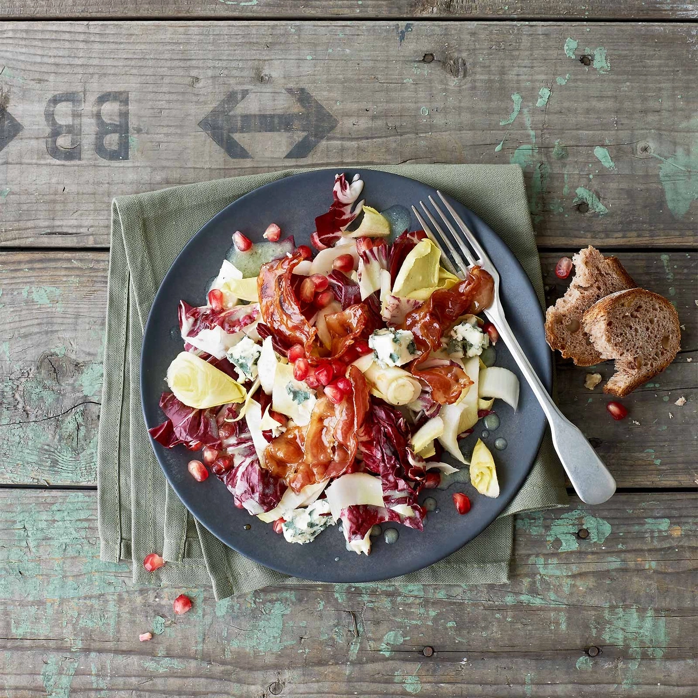 Salat mit Granatapfel, Käse, Schinken und Brot auf einem Teller.