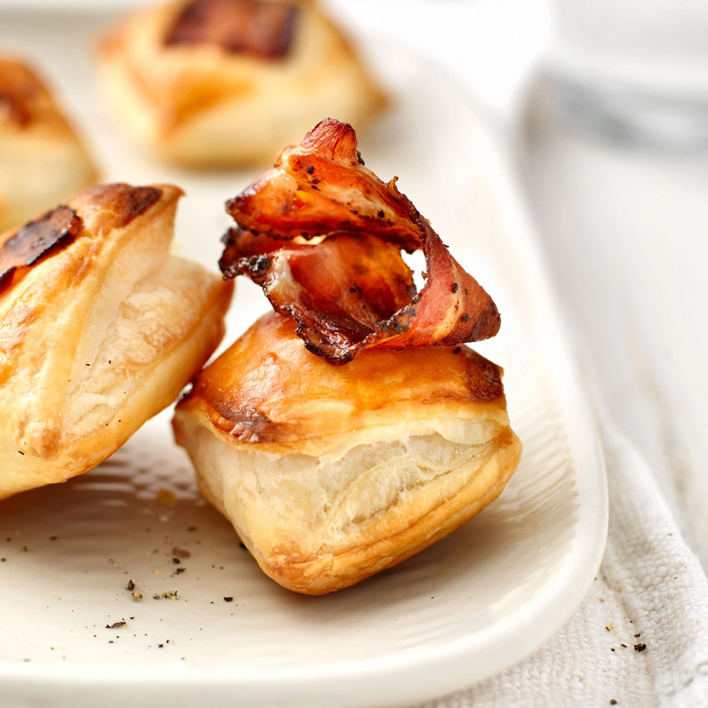 Délicieuses bouchées de pâte feuilletée avec du bacon croustillant sur une assiette blanche.