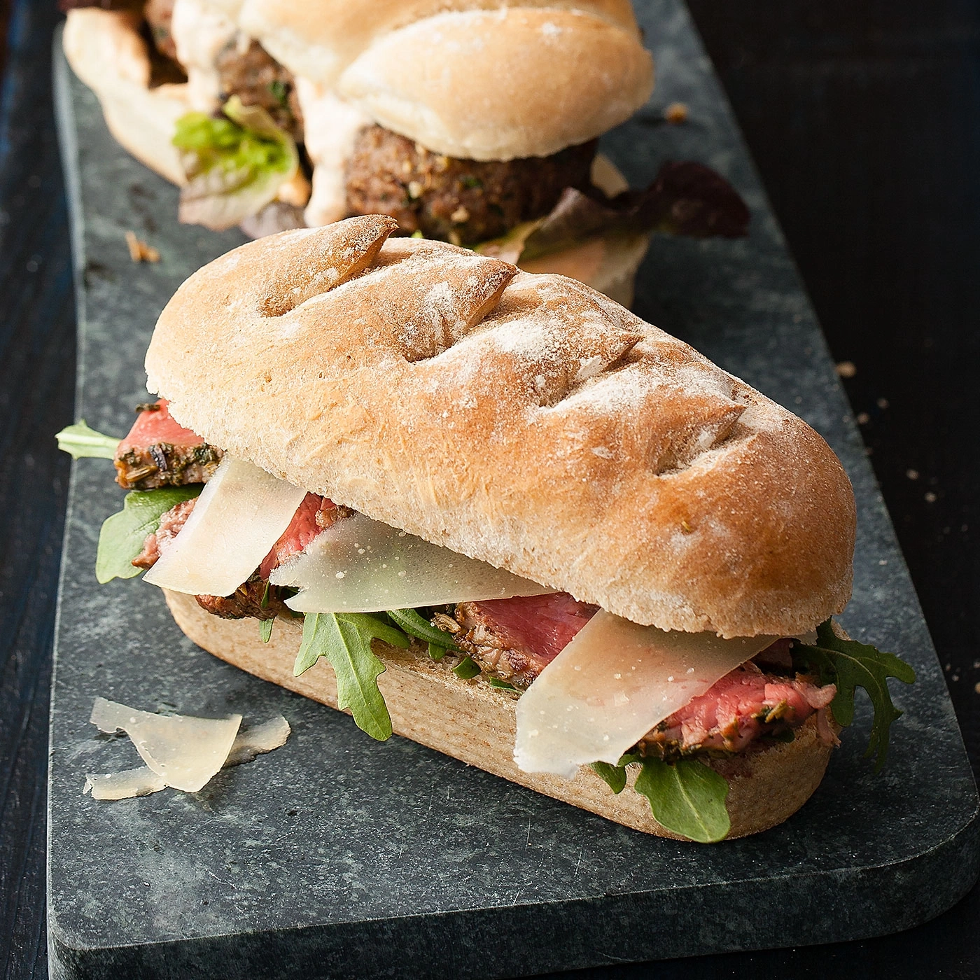 Sandwich mit Fleisch, Käse und Rucola auf einem Steinbrett