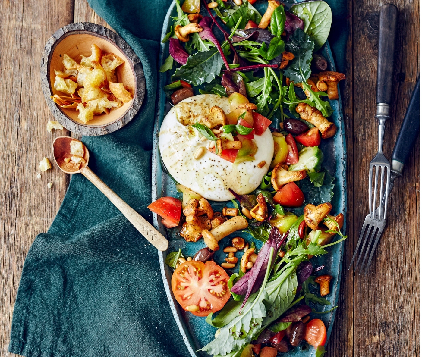 Köstlicher Salat mit Burrata, Tomaten, Pilzen und Croutons auf einem blauen Teller.