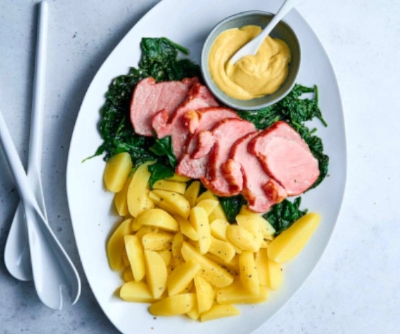 Gebratenes Fleisch mit Kartoffeln, Spinat und Senf auf einem Teller.