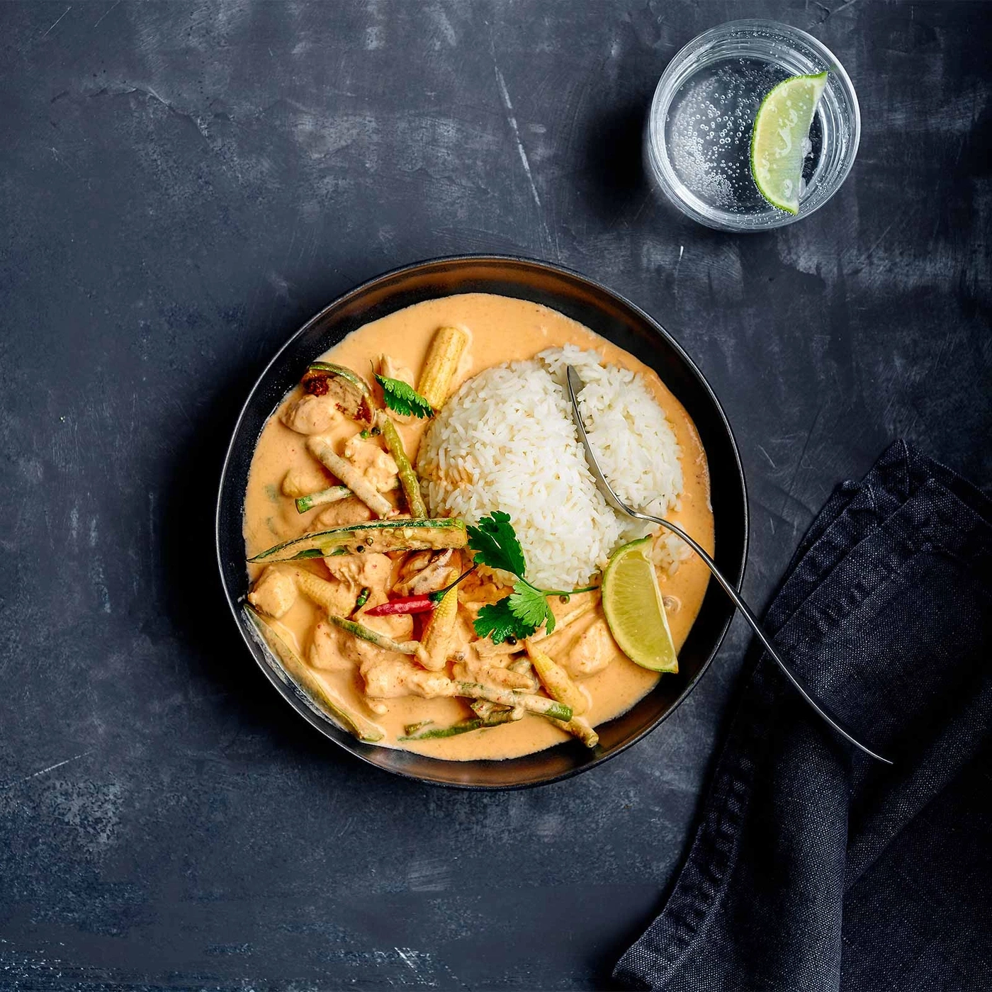 Asiatisches Gericht mit Reis, Curry, Gemüse und Limette auf dunklem Hintergrund.