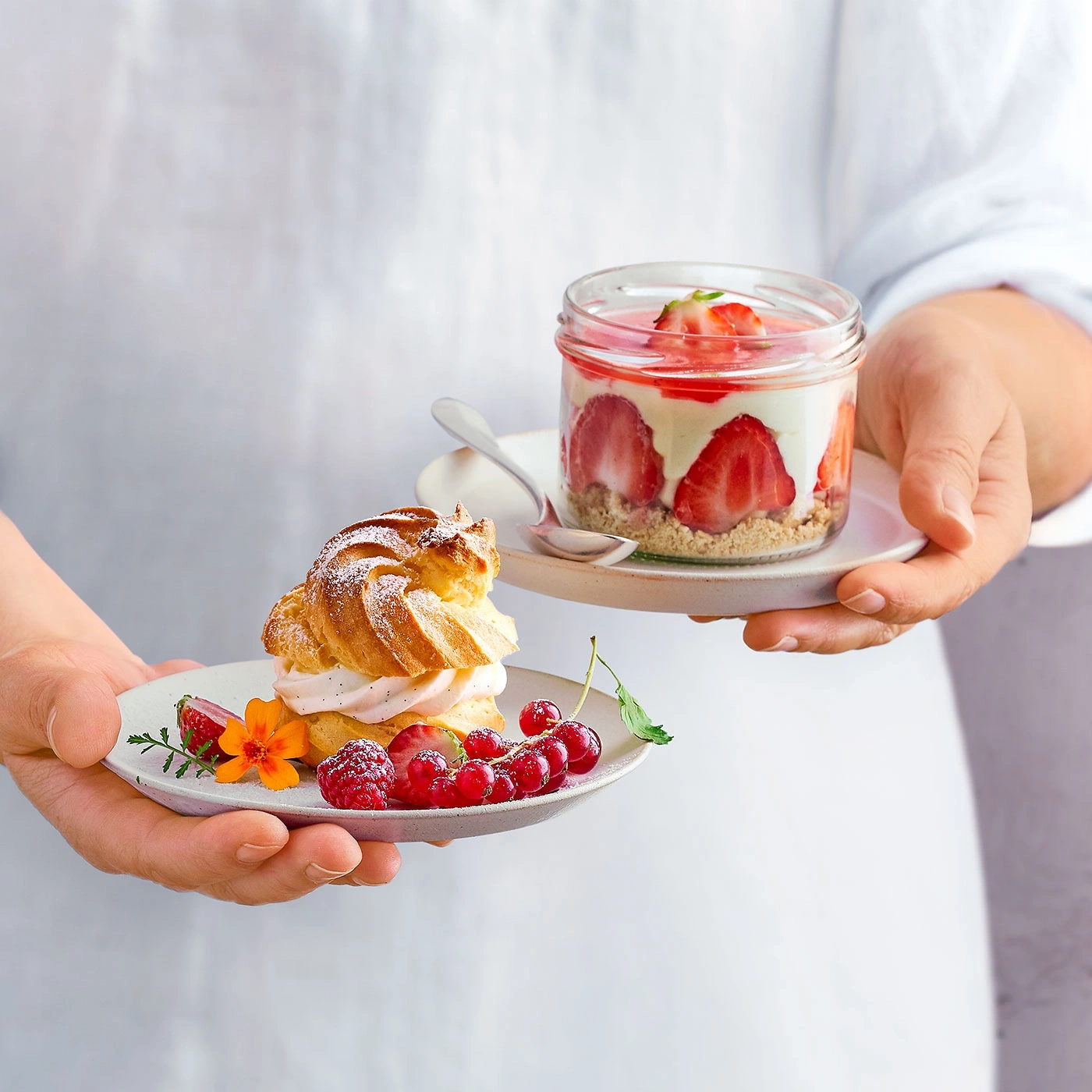 Person hält zwei Teller mit Desserts und Früchten. Lecker!