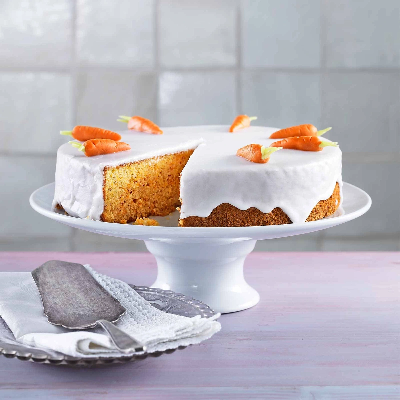 Karottenkuchen mit Zuckerguss und Karotten-Dekoration auf Tortenständer