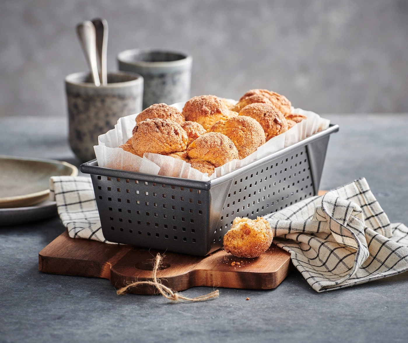 Köstliche Zimtschnecken in einem Korb auf einem Holzbrett mit Stoffserviette und Tassen.