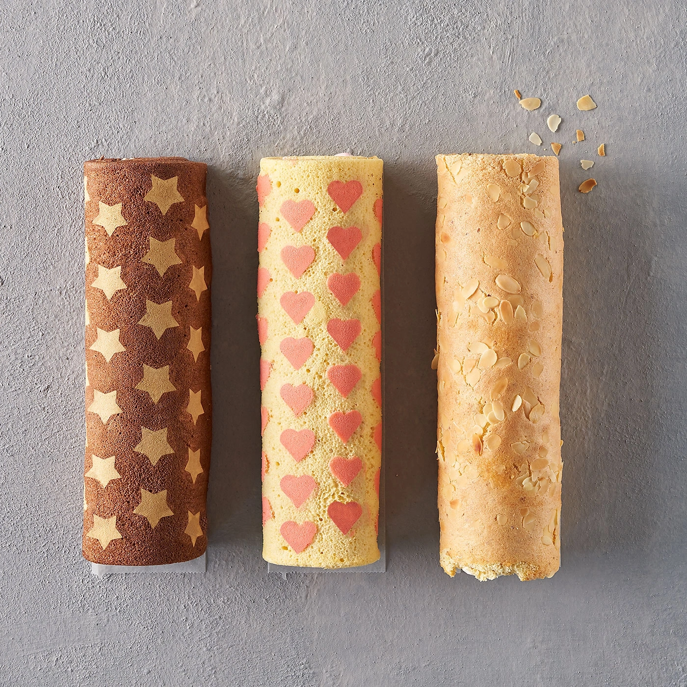 Trois roulés décorés d'étoiles, de coeurs et d'amandes sur fond gris.