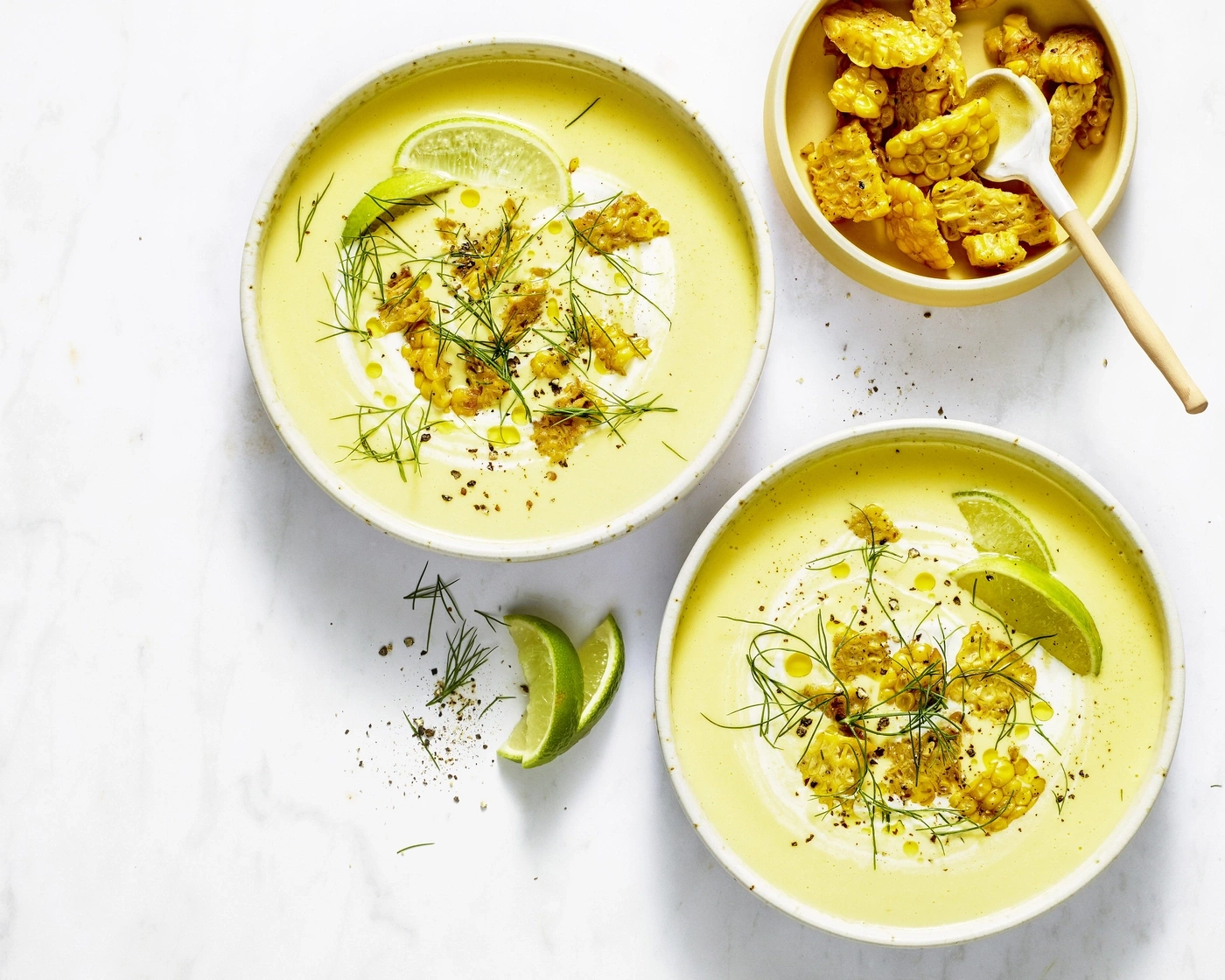Zwei Schüsseln cremiger gelber Suppe mit geröstetem Mais, Limette und Dill.