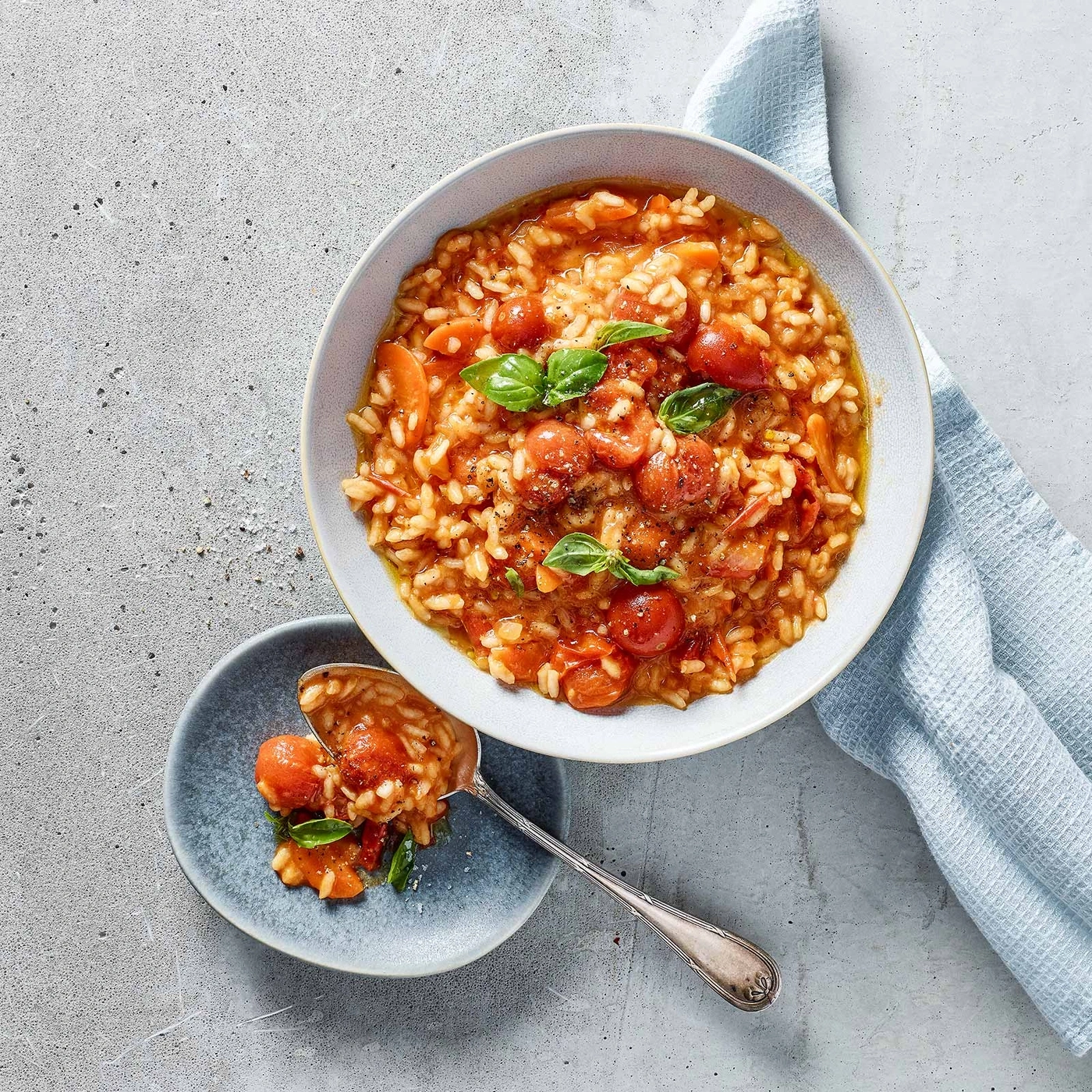 Tomaten-Risotto mit Basilikum, serviert in einer Schüssel und auf einem Teller.