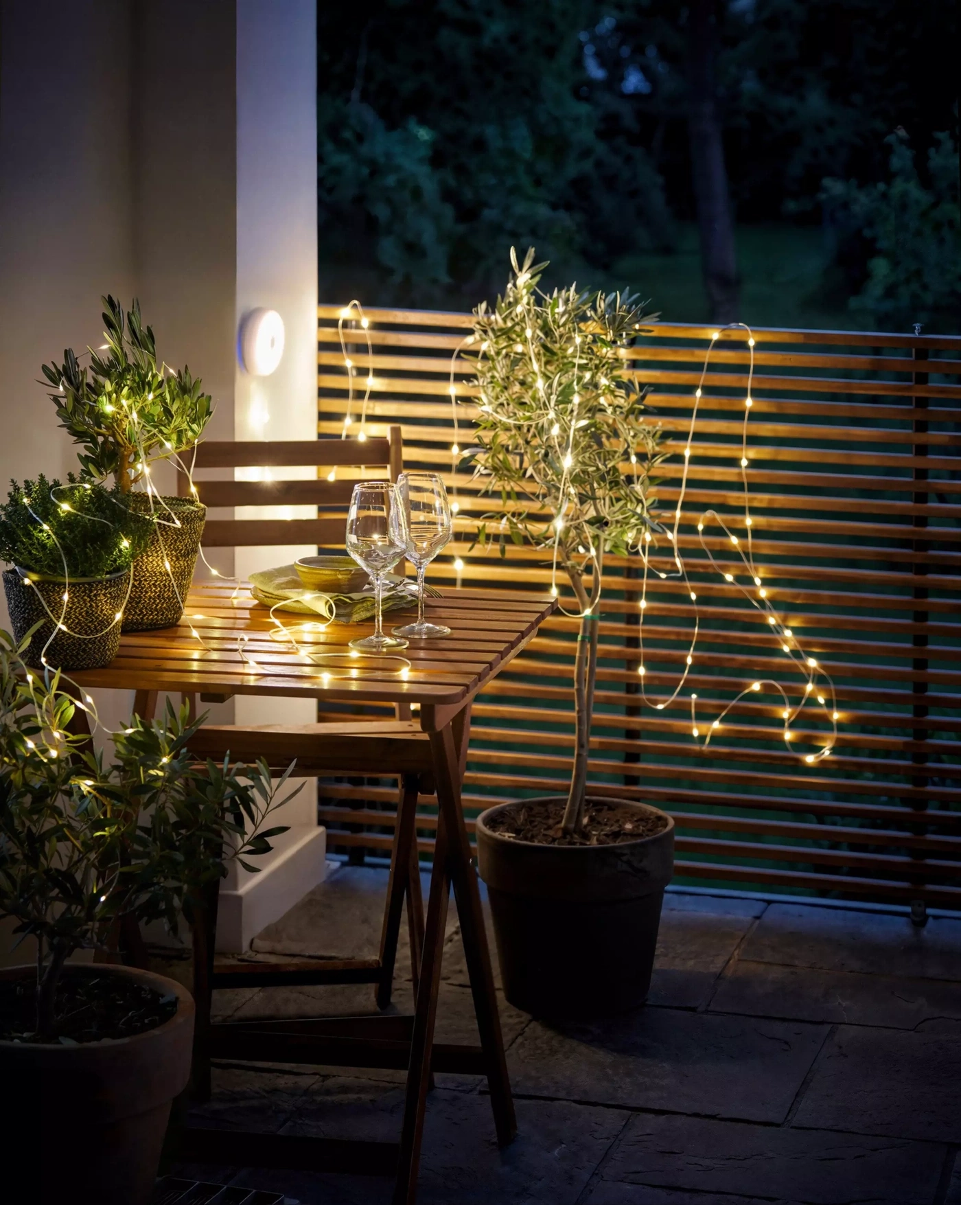 Table en bois avec verres à vin et guirlandes lumineuses sur une terrasse la nuit.