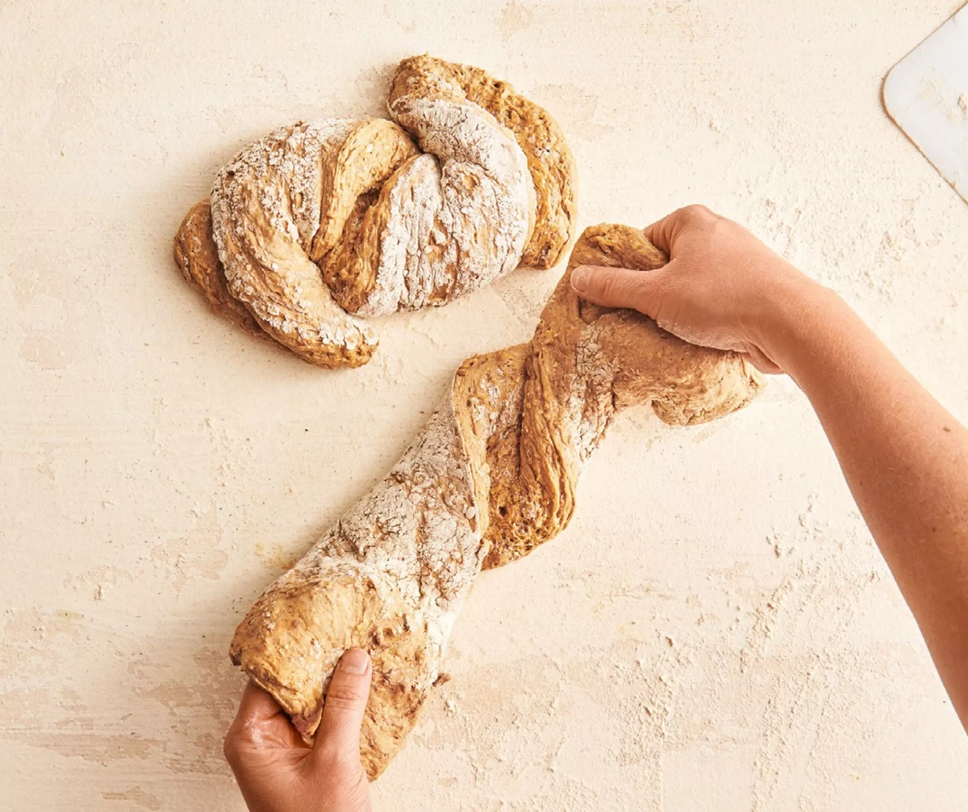 Mains façonnant une pâte à pain tressée sur une surface farinée.
