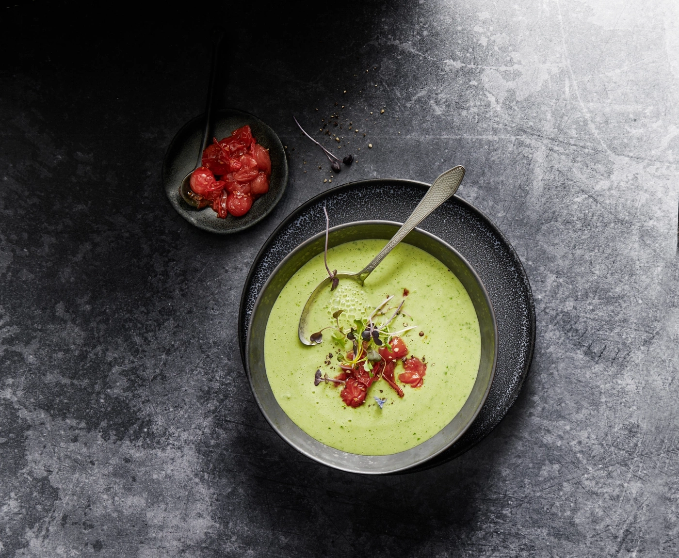 Grüne Suppe mit Tomaten und Kräutern auf dunklem Steinboden