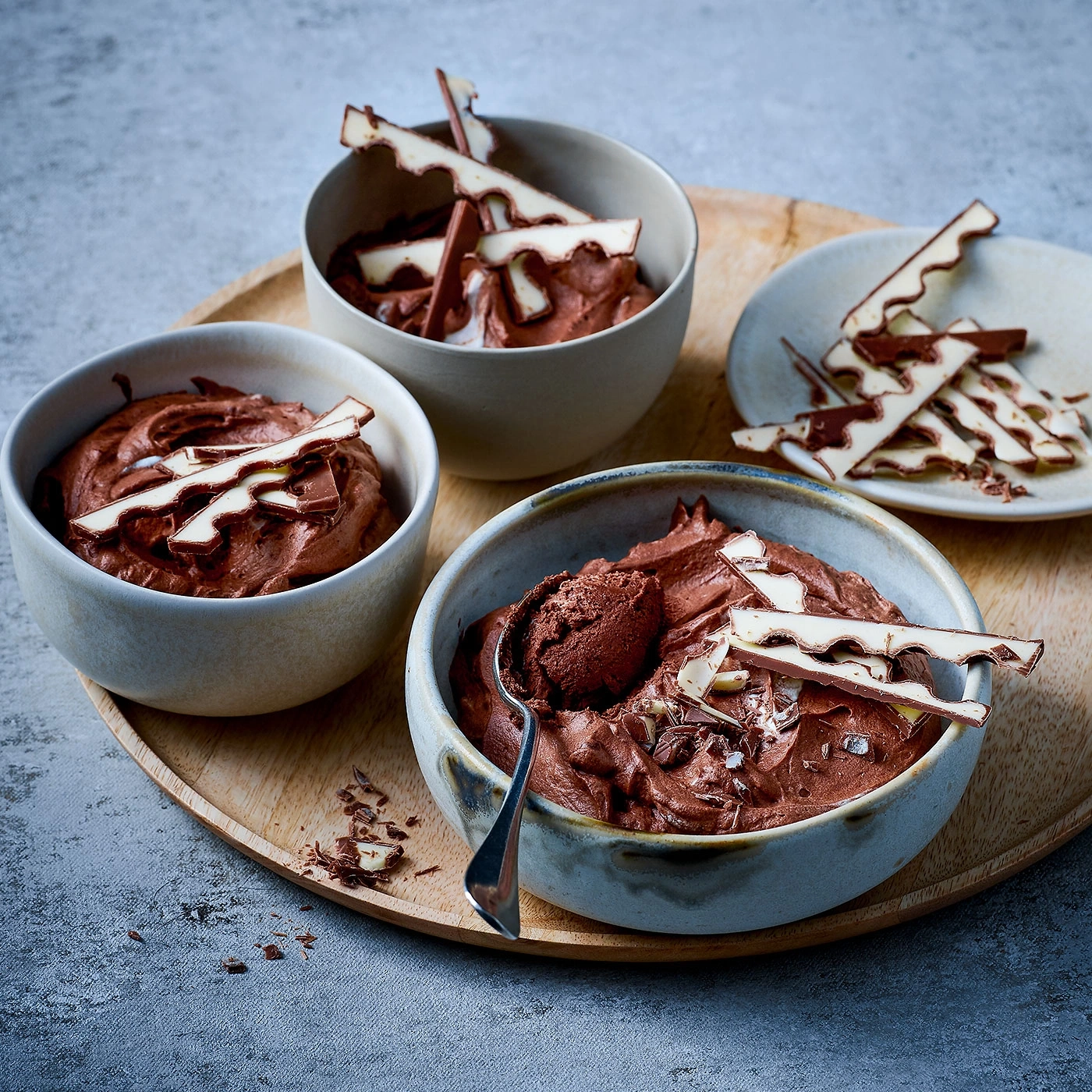 Schokoladenmousse in Schalen mit Schokoladenstückchen auf einem Holztablett.