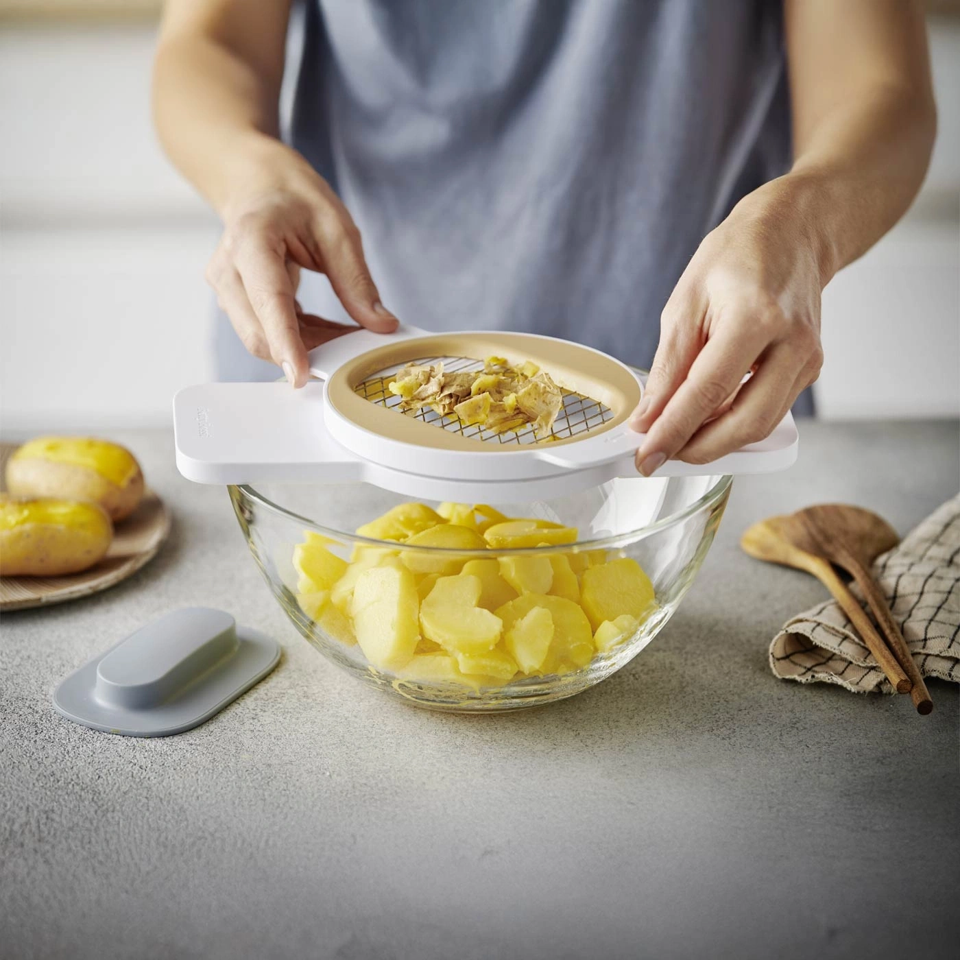 Person schneidet Kartoffeln mit einem Küchenwerkzeug in einer Glasschüssel.