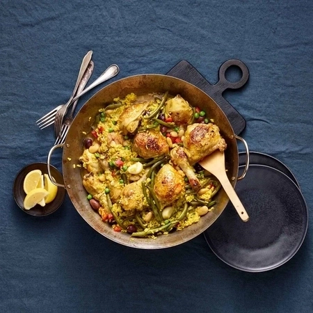 Paella mit Hühnchen, Gemüse und Zitrone auf einem blauen Tisch.