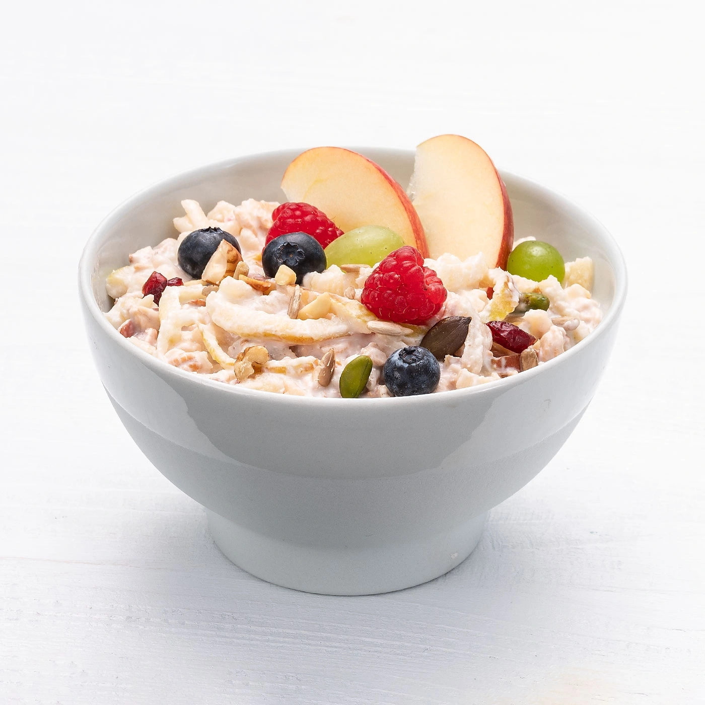 Eine Schüssel Müsli mit Obst, Nüssen und Samen auf weißem Hintergrund.