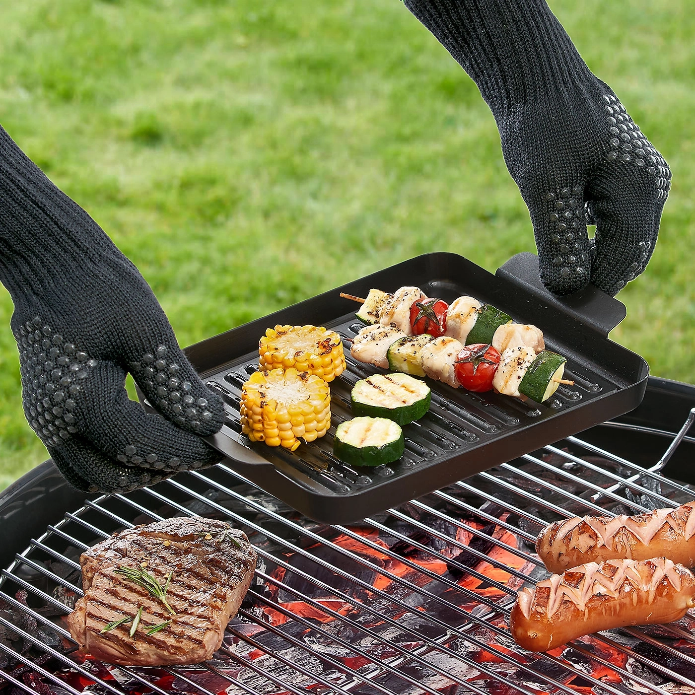Grillen mit Mais, Würstchen, Steak und Spießen. Hände mit Handschuhen.