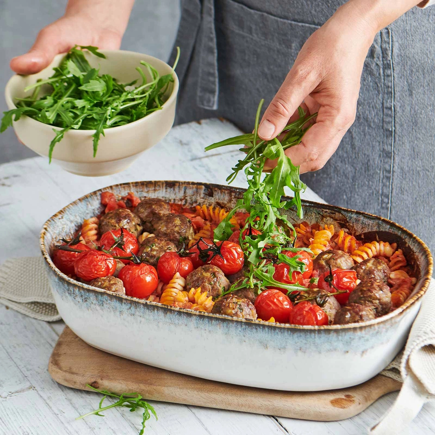 Person garniert Pasta mit Tomaten und Fleischbällchen mit Rucola.