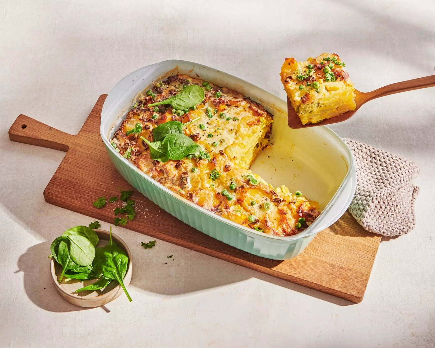 Gratin de pommes de terre avec pois et épinards sur une planche en bois