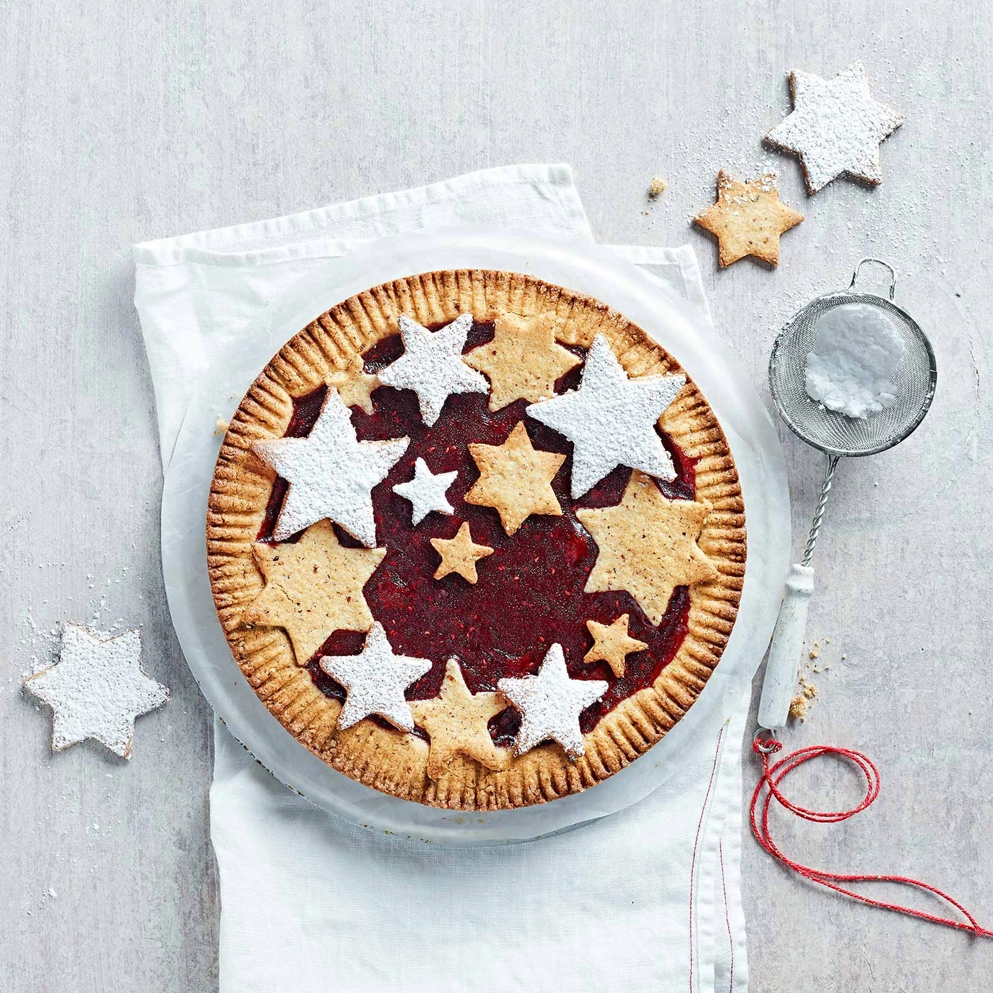 Sternförmiger Kuchen mit Puderzucker, auf weißem Tuch, mit Stern-Dekoration und Sieb.