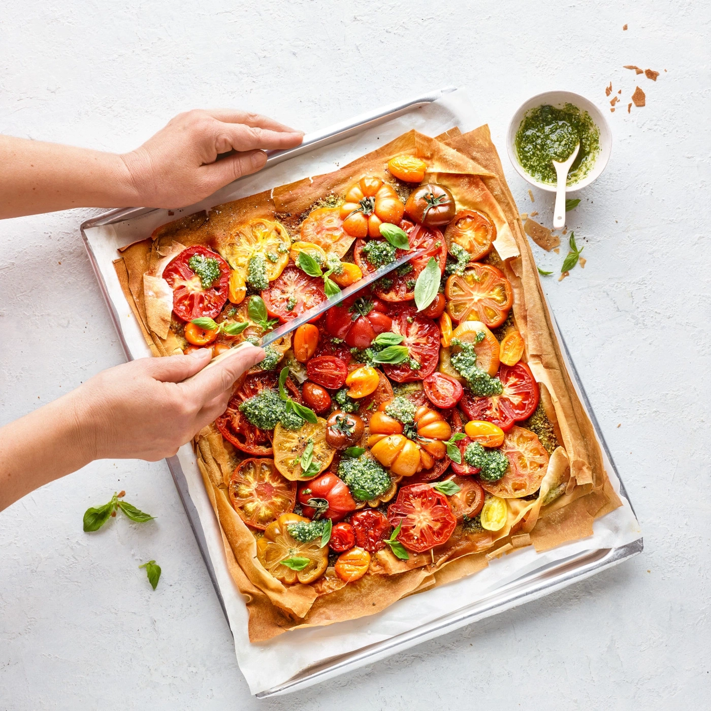 Tarte aux tomates sur plaque, coupée au couteau, basilic, pesto, plat