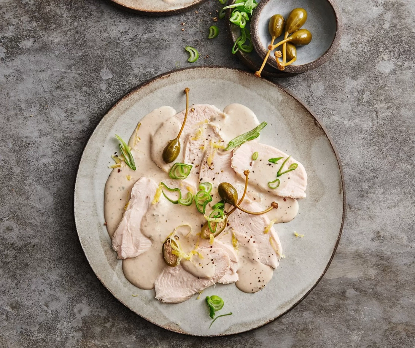 Viande cuite en tranches nappée de sauce avec des câpres sur une assiette