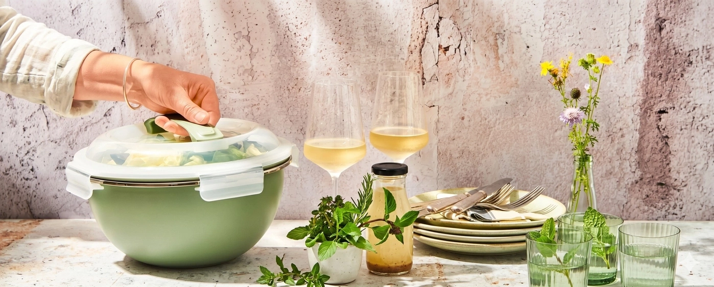Grüne Schüssel mit Salat, Wein und Kräutern auf Tisch