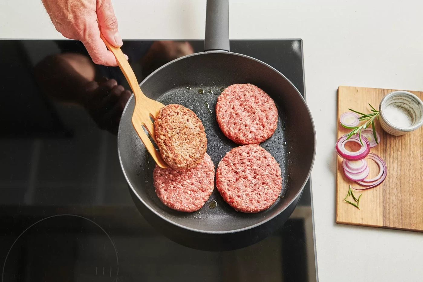 Galettes de viande cuites dans une poêle, avec des oignons et des épices à côté