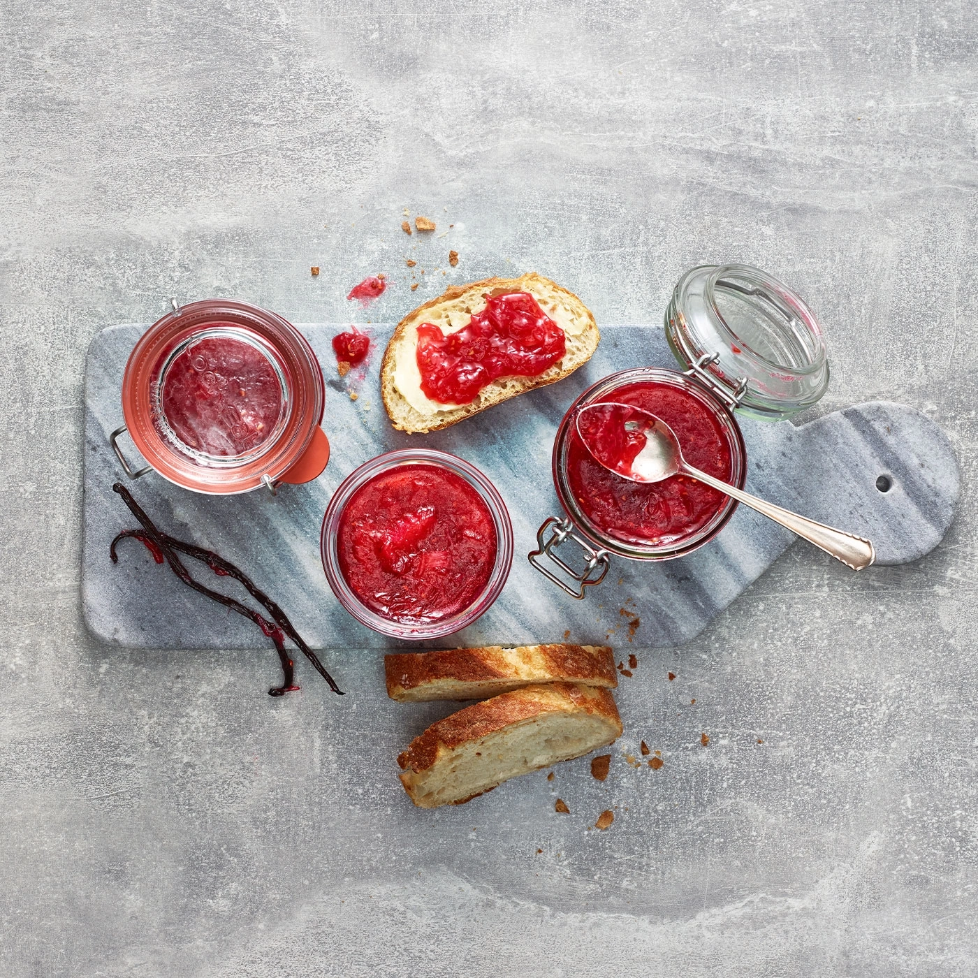 Erdbeermarmelade mit Brot, Gläsern und Vanilleschoten auf einem Brett