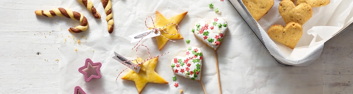 Weihnachtsplätzchen auf weißem Papier, Sterne, Herzen, Zuckerstreusel, Backblech