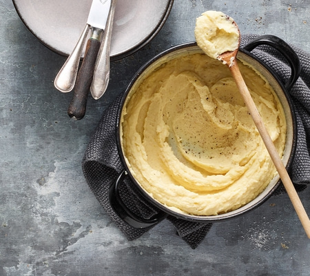 Purée de pommes de terre dans une casserole avec une cuillère et des couverts sur une table