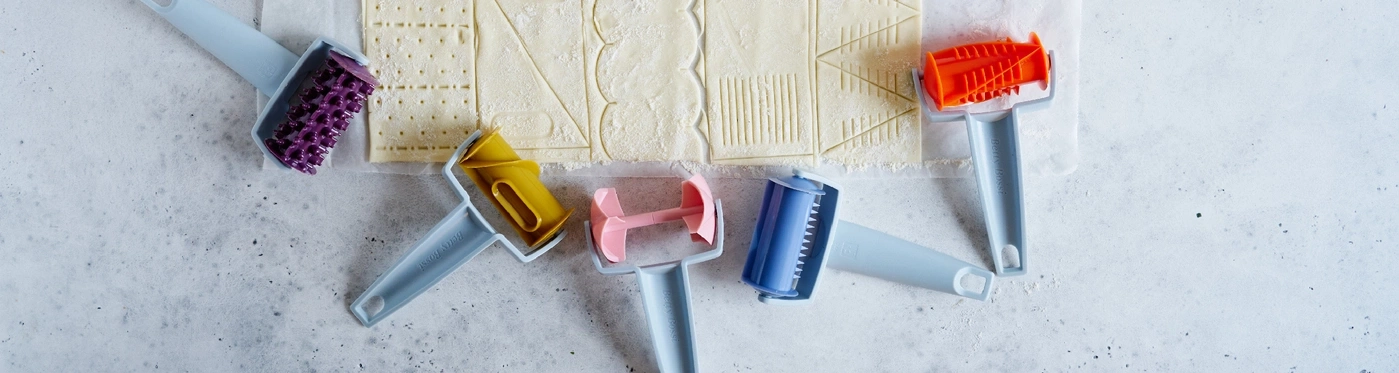 Divers rouleaux à pâtisserie sur une surface de travail avec de la pâte, ustensiles de cuisine.