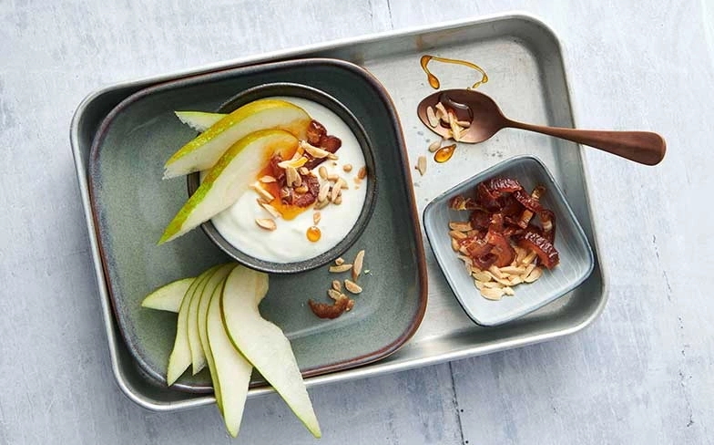 Yaourt avec poire, amandes et miel servi sur un plateau