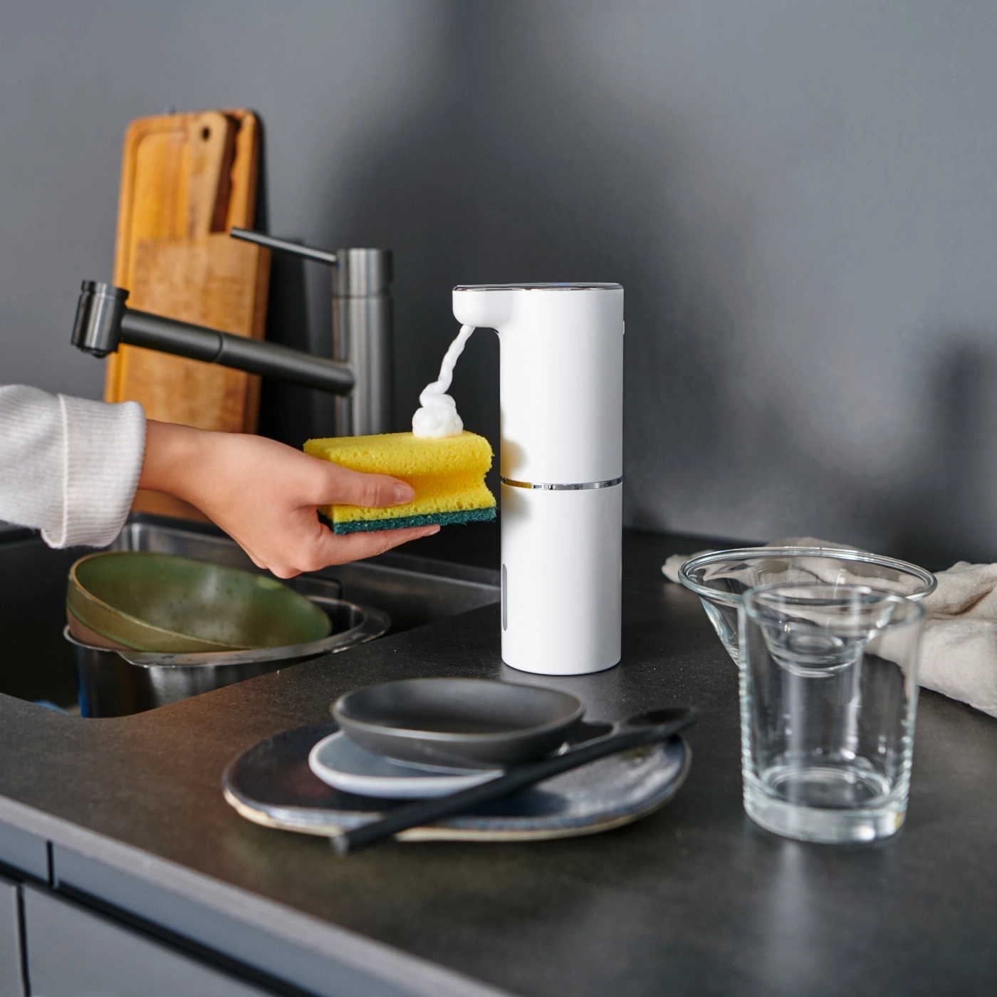 Personne utilisant une éponge avec du savon dans la cuisine pour faire la vaisselle.