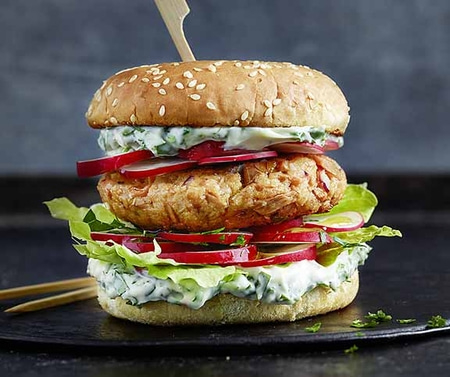 Burger mit Radieschen, Salat und Sauce auf einem schwarzen Teller.